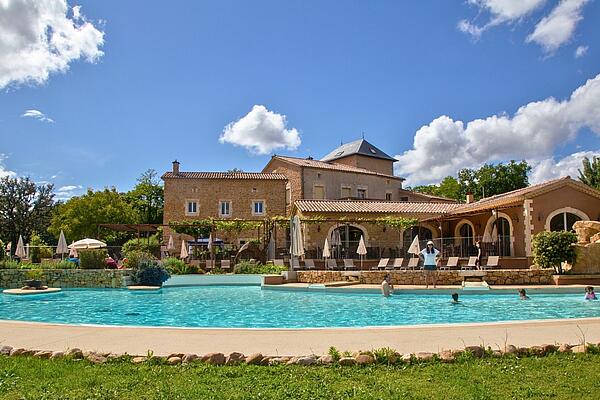 Historic estate pool at Castels Domaine de Sévenier, Ardèche, France. Swimmers enjoying the outdoor pool in front of the historic stone building at Castels camping Domaine de Sévenier.