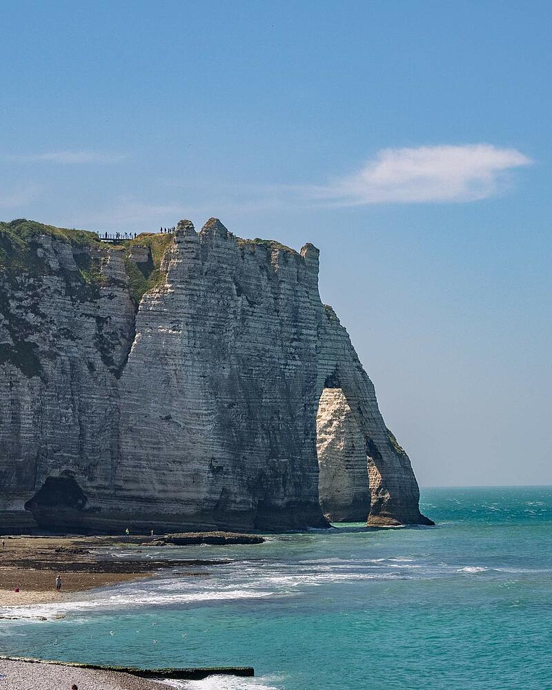 A vertical shot of the famous towering white chalk cliffs and natural arch of Étretat, with waves crashing onto the beach, located near a Les Castels camping resort.