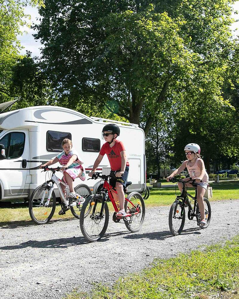 Children riding bikes past motorhomes at a luxury campsite near Calais, illustrating the safe and spacious environment for a stopover in France.