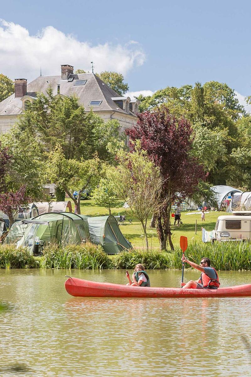 Vacances en camping en France : balade en canoë sur une rivière devant un domaine avec château et tentes