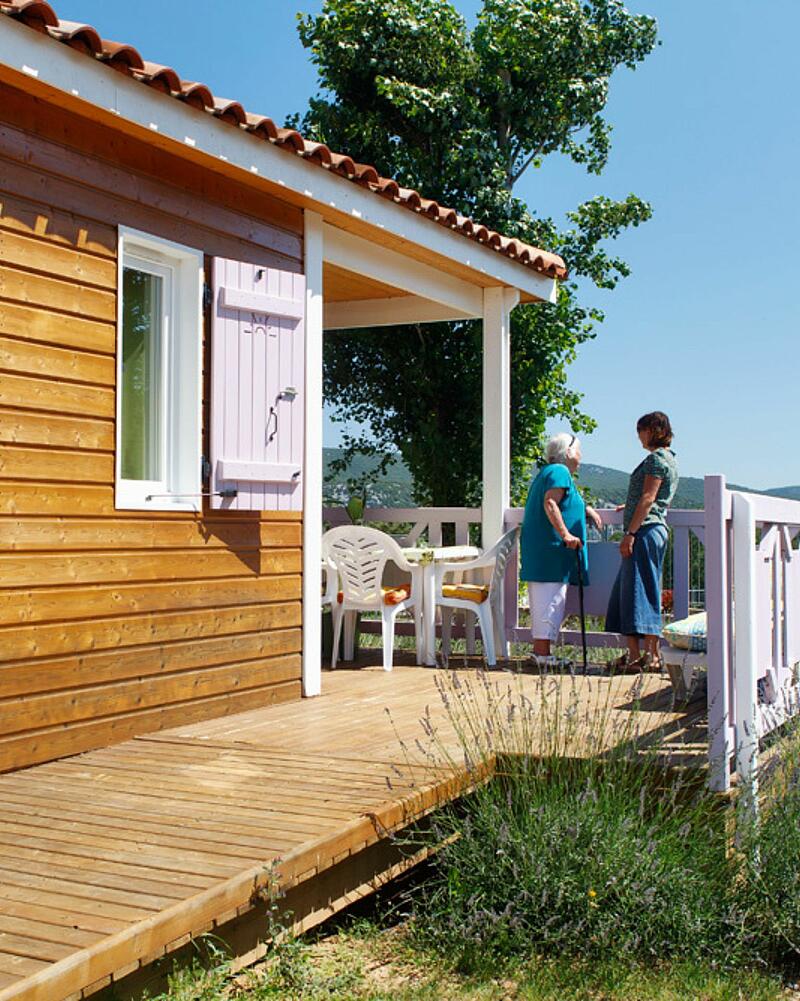 Two women relaxing on the wooden terrace of a premium chalet at Les Castels luxury campsite in Ardeche.