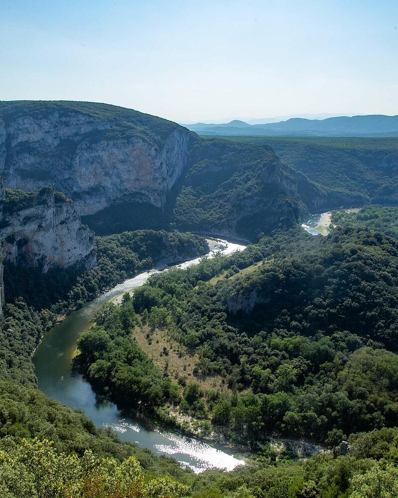 Panoramic high angle view of the green Ardeche river canyon winding through deep forests and massive stone cliffs near Les Castels campsites.