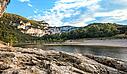 Panoramic view from a rocky outcrop across the quiet Ardeche river towards massive Ardeche Gorges cliffs and green forests, typical of the natural environment near a 5-star Les Castels estate.