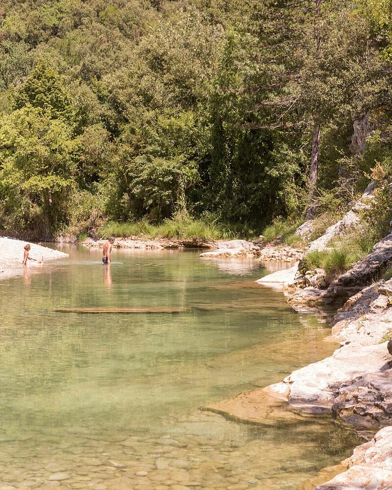 People relaxing and swimming in the clear waters of a wild river near Les Castels luxury campsites in Ardèche, France.