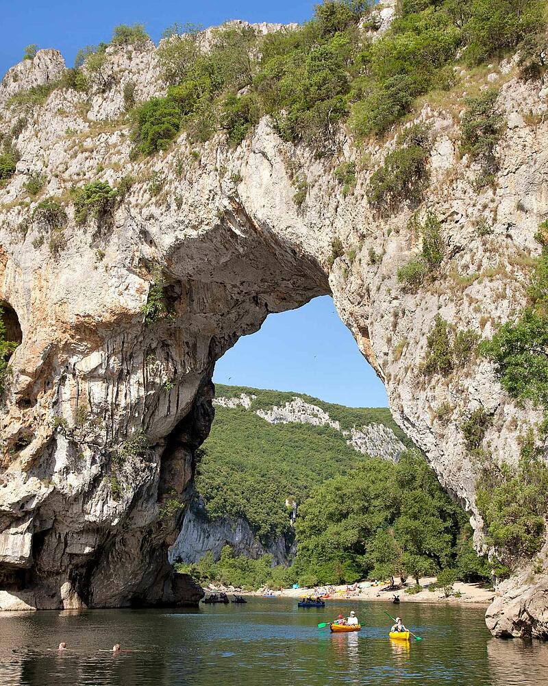 Kayaks and canoes floating on the river under the massive, natural limestone arch of the Pont d'Arc in the spectacular Ardèche Gorges.