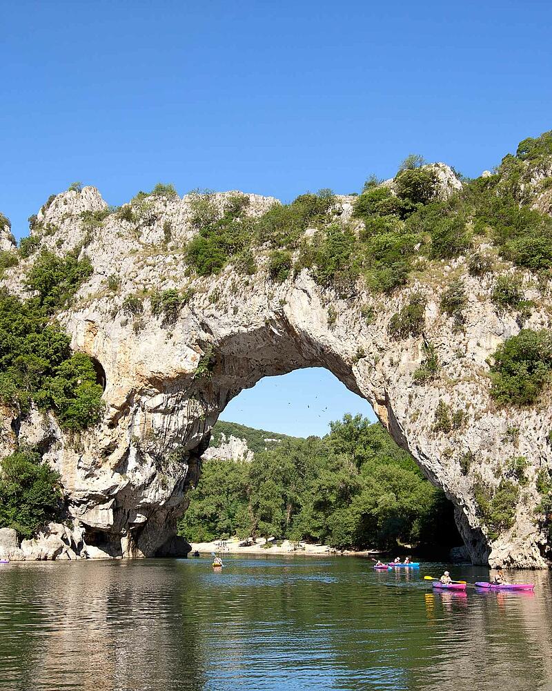 Colorful holidaymakers paddling on kayaks and canoes on the river right underneath the giant natural stone bridge of Pont d Arc near Les Castels luxury campsites.