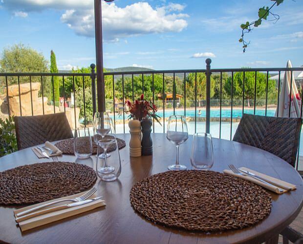 Restaurant table with a pool view at Castels Domaine de Sévenier, Ardèche, France. A beautifully set dining table on the terrace overlooking the outdoor pool at Castels camping Domaine de Sévenier.