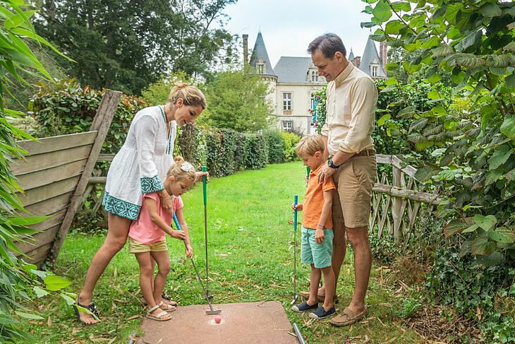 une famille jouant au mini-golf devant le château de la ville-huchet