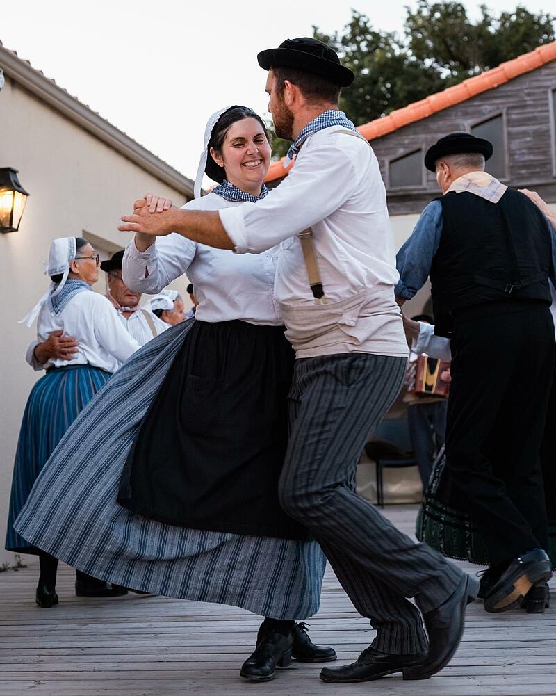Dancers dressed in historic regional attire performing traditional choreography on an outdoor wooden floor during a cultural event at a Les Castels campsite.