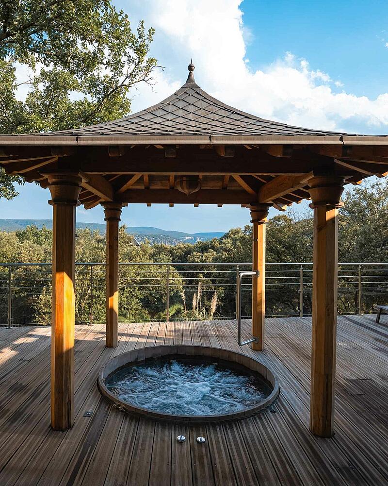 Outdoor jacuzzi under a wooden gazebo overlooking the valley at Les Castels Domaine de Sévenier spa campsite in Ardeche.