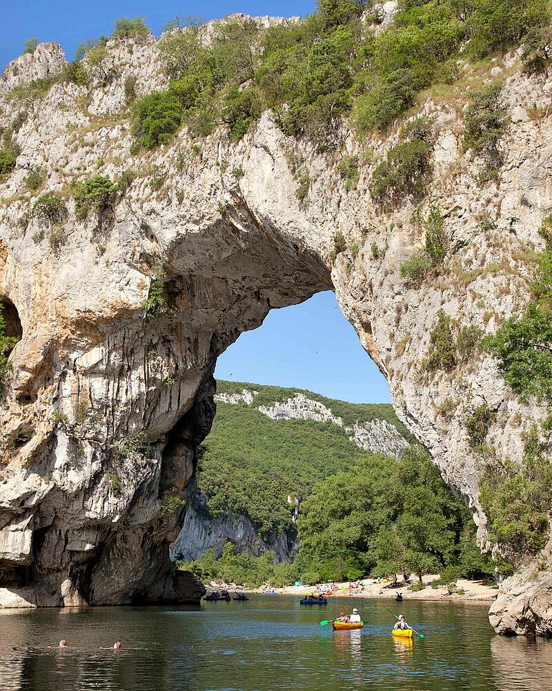 Kayakers and swimmers at the famous Pont d'Arc natural stone bridge in the Ardèche Gorges near Les Castels estate campsites.