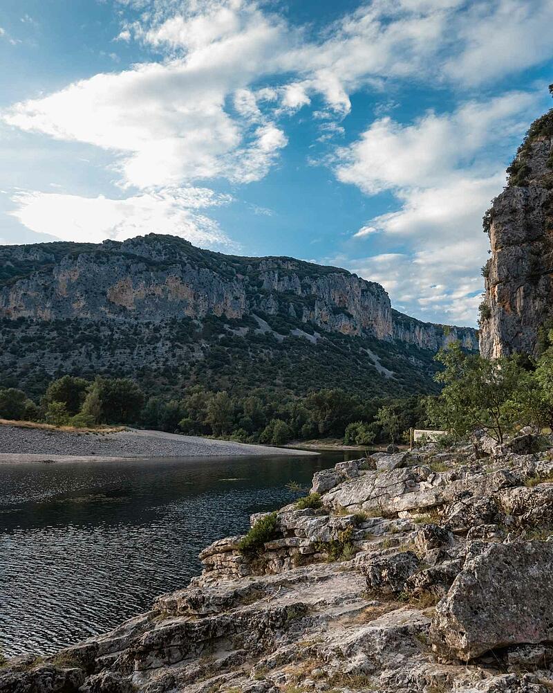 Breathtaking river canyon view near Castels Domaine de Sévenier, Ardèche, France. High limestone cliffs tower over a winding river with a rocky shore in the landscape near Castels camping Domaine de Sévenier.