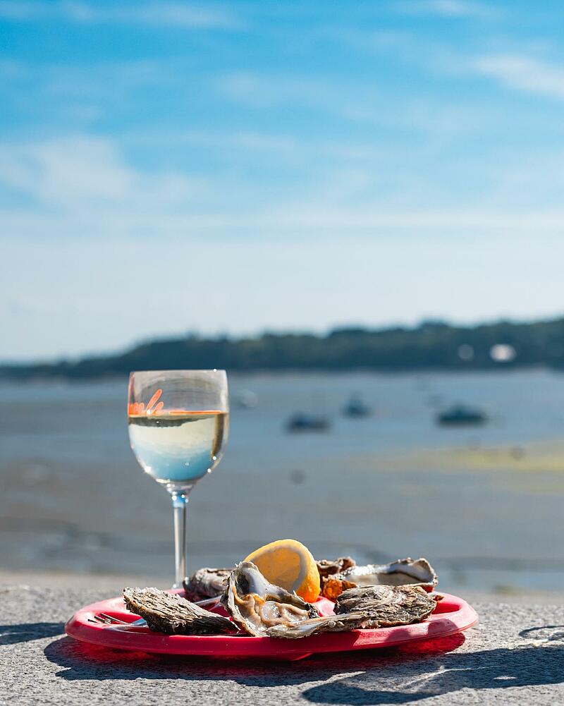 A platter of fresh oysters with lemon and a glass of white wine on a stone wall overlooking the ocean at Cancale, Brittany.