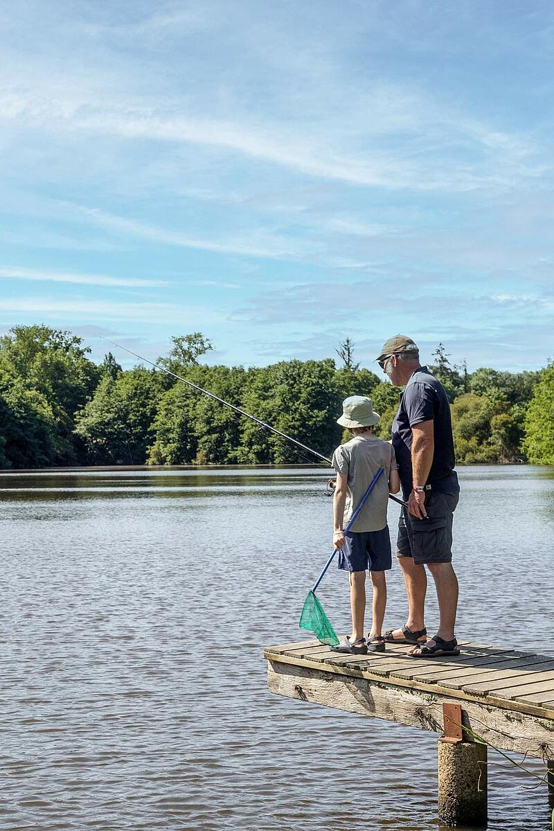 Activité de pêche en famille lors d'un séjour en camping en France, sur un ponton en bois face à un lac entouré d'arbres.
