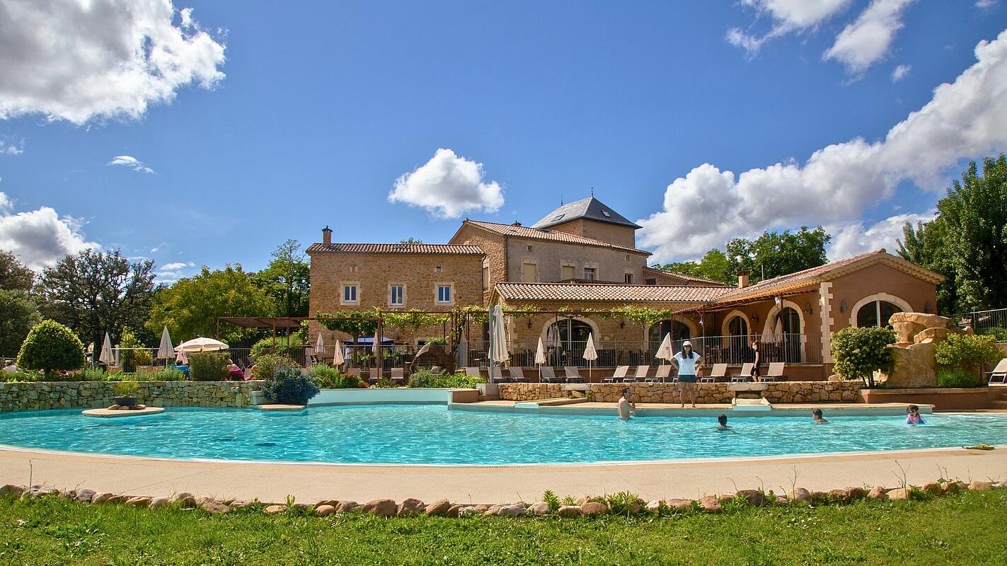 Historic estate pool at Castels Domaine de Sévenier, Ardèche, France. Swimmers enjoying the outdoor pool in front of the historic stone building at Castels camping Domaine de Sévenier.