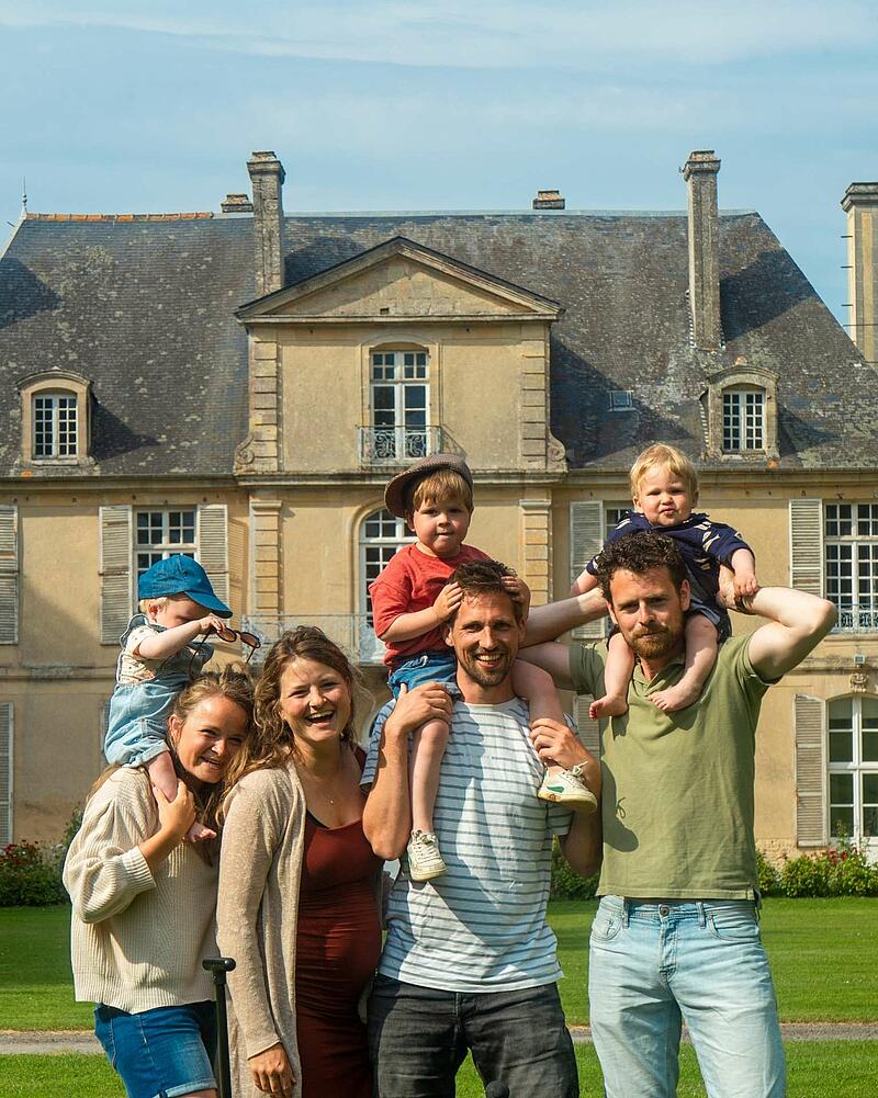 A joyful group photo of adults and young children smiling together in front of a historic French chateau at a luxury Les Castels holiday estate.