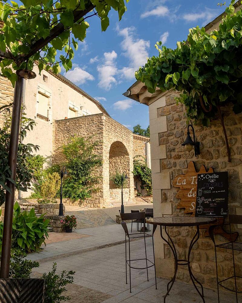 Charming stone village courtyard with a restaurant cocktail menu board at Les Castels Domaine de Sévenier in Ardèche.