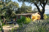 A premium wooden cottage with a private garden terrace, sun loungers, and lavender bushes under large trees at an upscale Les Castels campsite in France.